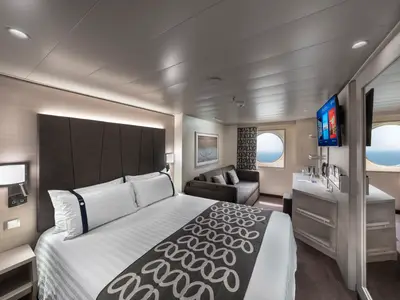 Eine helle Deluxe Aussenkabine an Bord der MSC Euribia mit grosszügigem Doppelbett, Sofa, TV und zwei runden Fenstern mit Meerblick. Die Kabine ist modern und elegant eingerichtet.