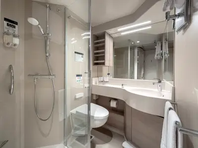 Ein helles, modernes Badezimmer an Bord der MSC Euribia mit einer Duschkabine, WC, Waschbecken und grosser Spiegelfront. Weiße Handtücher hängen bereit.