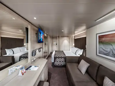 Eine helle und modern eingerichtete Deluxe-Kabine an Bord der MSC Euribia. Sie zeigt ein komfortables Doppelbett, ein Sofa, einen Fernseher und einen Schminktisch.