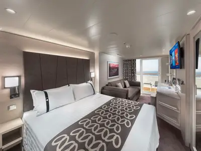 Die moderne Deluxe Balkonkabine der MSC Euribia zeigt ein großes Doppelbett, eine Sitzecke mit Sofa, einen Schreibtisch und einen Balkon mit weitem Meerblick.