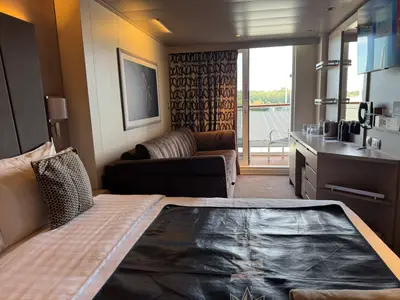 Innenansicht einer modernen Balkonkabine an Bord der MSC Euribia mit Bett, Sofa und Blick auf den Balkon.