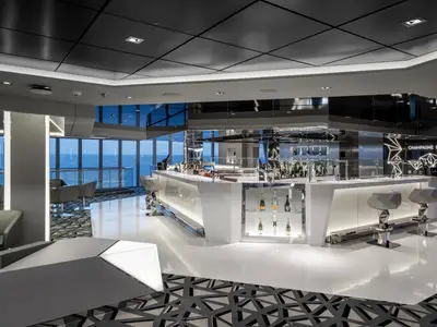 Elegante Champagne Bar an Bord der MSC Euribia. Modernes Interieur in Grau und Weiß, große Fenster mit Meerblick. Die Bar ist mit Champagnerflaschen und Designer-Barhockern ausgestattet.