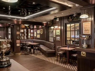Die Masters of the Sea Bar an Bord der MSC Euribia. Ein gediegener Innenbereich im Pub-Stil, geprägt von dunklem Holz, Ledersitzbänken und kleinen Tischen. Gerahmte Bilder und Trophäen, wie ein großer silberner Pokal, schmücken den Raum.