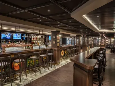 Die Masters of the Sea Bar an Bord der MSC Euribia. Holztheke mit Bierhähnen und Barhockern. Dunkles Holz und warmes Licht schaffen eine klassische Pub-Atmosphäre mit Sitzbereichen.