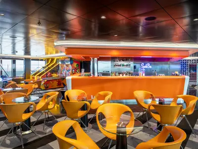 Lebhafte Sports Bar an Bord der MSC Euribia. Auffällig orange Theke, moderne Stühle, kleine Tische und Arcade-Spiele füllen den Raum. Große Fenster bieten Meerblick.