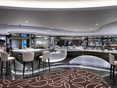 Blick auf die moderne Infinity Bar an Bord der MSC Euribia mit einer geschwungenen, beleuchteten Theke, Barhockern und einer gut bestückten Spirituosenwand.