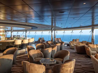 Blick in die elegante Sky Lounge an Bord der MSC Euribia mit einer gut sortierten Bar, bequemen Sesseln und Panoramafenstern zum Meer.