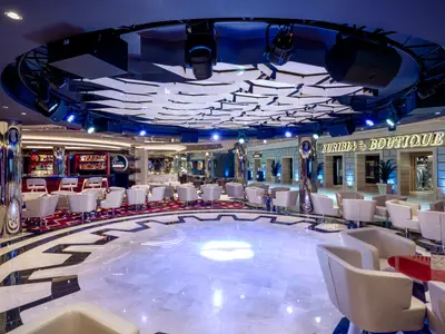 Die Euribia Bar & Lounge an Bord der MSC Euribia zeigt eine kreisförmige Tanzfläche, umgeben von weissen Sesseln. Im Hintergrund eine Bar und die Euribia Boutique.