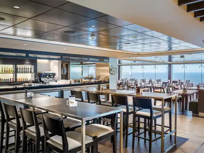 Ein weitläufiger Buffetbereich mit zahlreichen Tischen, Stühlen und einer gut ausgestatteten Bar an Bord der MSC Euribia. Große Fenster bieten einen weiten Blick auf das offene Meer.