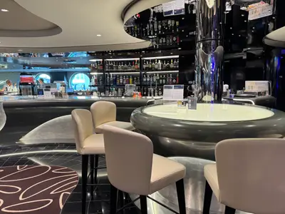 Barbereich an Bord der MSC Euribia mit modernen Barhockern, einem runden Designtisch und einer gut sortierten Bar mit Flaschen im Hintergrund.