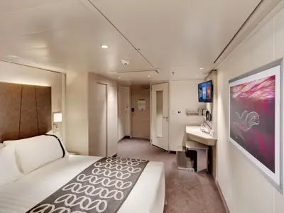 Innenansicht einer barrierefreien Kabine an Bord der MSC Euribia mit Doppelbett, Schrank und Schreibtischbereich. Moderne, helle Einrichtung und Kunst an der Wand.