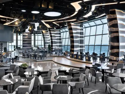 Moderne Carousel Lounge an Bord der MSC Euribia mit Bühne und Musikinstrumenten. Bequeme Sitzgruppen und große Panoramafenster bieten weiten Meerblick.