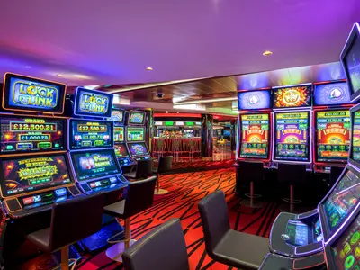 Eine weitläufige Ansicht des MSC Signature Casinos an Bord der MSC Euribia. Zahlreiche helle Spielautomaten mit leuchtenden Bildschirmen und roten Akzenten säumen den Raum, während im Hintergrund eine stilvolle Bar mit Barhockern zu sehen ist. Der Boden ist mit einem auffälligen roten Teppich mit schwarzen Mustern bedeckt.