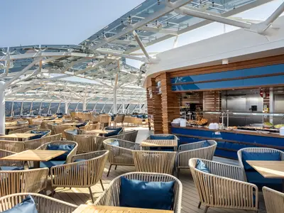 Der helle Buffetbereich an Deck der MSC Euribia mit zahlreichen Tischen und Stühlen unter einem modernen Glasdach. Im Hintergrund ist eine Buffetauslage mit Speisen sichtbar.