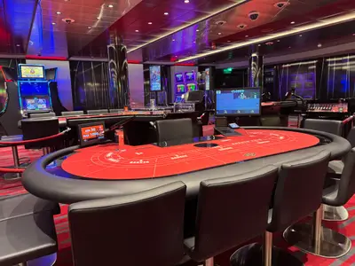 Blick auf einen großen roten Baccara-Spieltisch und Spielautomaten im eleganten Casino an Bord der MSC Euribia.