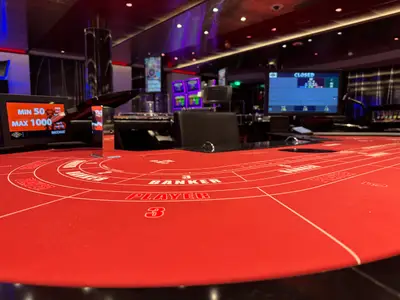 Ein roter Baccarat-Spieltisch im modernen Casino an Bord der MSC Euribia mit Bildschirmen im Hintergrund.