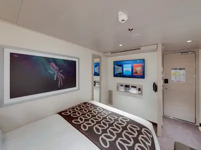 Blick in eine moderne Innenkabine der MSC Euribia mit Doppelbett, Flachbildfernseher, Kunstwerk und Spiegel. Helle Möbel, minimalistisches Design. Ohne Personen.
