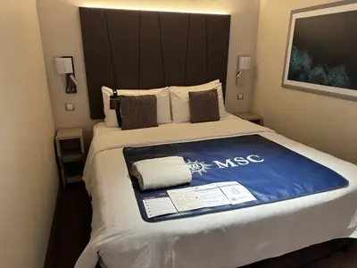 Doppelbett in einer gemütlichen Innenkabine an Bord der MSC Euribia mit MSC-Bettläufer und Handtüchern.