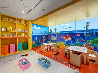 Der farbenfrohe LEGO-Mini-Club an Bord der MSC Euribia. Regale mit LEGO-Figuren, Bausteinen. Maritime Wandbilder: Meerjungfrauen, Piraten. Spieltische und LEGO-Eisenbahn am Boden.