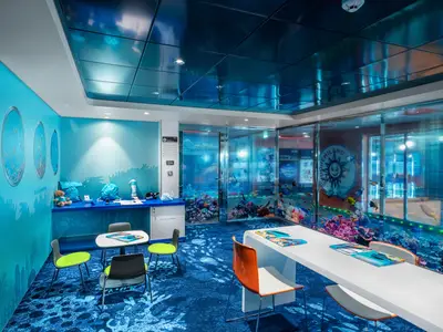 Das MSC Foundation Lab an Bord der MSC Euribia, ein Kinderbereich mit Unterwasser-Design. Hellblaue Wände, Bullaugen mit Fischmotiven und eine Korallenriff-Glaswand. Kleine Tische und Stühle für Kinder.