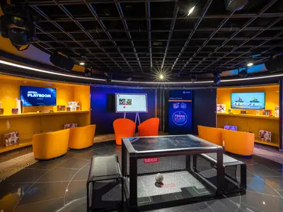 Moderner Teen Club an Bord der MSC Euribia mit Gaming-Stationen, orangefarbenen Sesseln und Subsoccer-Tisch. Ideal für Jugendliche.