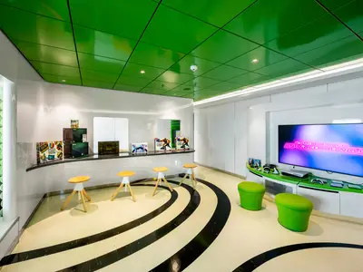 Der moderne Young Club an Bord der MSC Euribia. Der Raum ist in Weiss und leuchtendem Grün gehalten und verfügt über Gaming-Konsolen, einen grossen TV-Bildschirm und Sitzgelegenheiten für junge Passagiere.