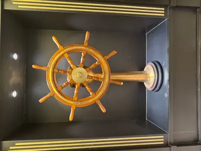 Ein klassisches hölzernes Steuerrad auf einem Messingständer, ausgestellt in einer beleuchteten Nische an Bord der MSC Euribia.