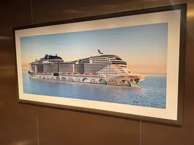 Ein gerahmtes Bild an der Wand zeigt das moderne Kreuzfahrtschiff MSC Euribia auf dem Meer im sanften Licht des Sonnenuntergangs.