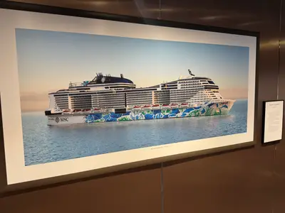 Ein gerahmtes Ausstellungsbild des Kreuzfahrtschiffs MSC Euribia mit aufwendiger Rumpfbemalung an einer braunen Wand.