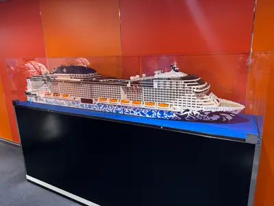 Ein großes, farbenfrohes LEGO-Modell des Kreuzfahrtschiffs MSC Euribia steht in einer Glasvitrine vor orangefarbenem Hintergrund.