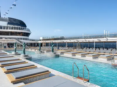 Ein weitläufiger Outdoor-Poolbereich an Deck der MSC Euribia mit azurblauem Wasser, umgeben von modernen Liegeflächen und dekorativen Kaktus-Skulpturen, unter strahlend blauem Himmel. Eine Treppe führt zu den oberen Decks des Schiffes.
