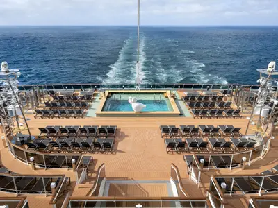 Weitläufiges Sonnendeck achtern der MSC Euribia: Horizon Pool, umgeben von Liegestühlen. Eine weiße Skulptur schmückt den Pool. Im Hintergrund das weite Meer mit Kielwelle.