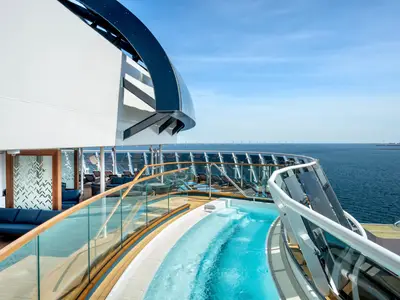 Sonnendeck der MSC Euribia mit Whirlpool, eleganten Lounge-Möbeln und Holzverkleidung. Im Hintergrund erstreckt sich das weite Meer mit vielen Windkraftanlagen am Horizont.