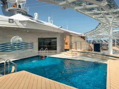 Ein sonniger Poolbereich auf dem Oberdeck der MSC Euribia mit einem tiefblauen Pool, umgeben von einem hellen Holzdeck und einer modernen Überdachung.