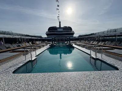Blick über den symmetrisch gestalteten Außenpool an Bord der MSC Euribia, umgeben von Liegestühlen unter blauem Himmel.