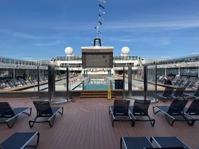Blick über das sonnige Pooldeck an Bord der MSC Euribia mit Sonnenliegen, einem Pool und einer großen Leinwand.