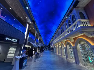 Die beleuchtete Innenpromenade Galleria Euribia an Bord der MSC Euribia mit einem leuchtend blauen LED-Himmel und klassischer Architektur.