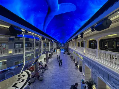 Blick auf die mehrstöckige Promenade an Bord der MSC Euribia mit Geschäften und einem riesigen LED-Himmel, der eine blaue Unterwasserwelt zeigt.