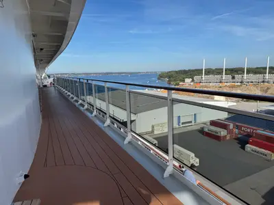 Blick von der Promenade an Bord der MSC Euribia auf einen Hafen mit Containern und das offene Meer bei klarem Himmel.