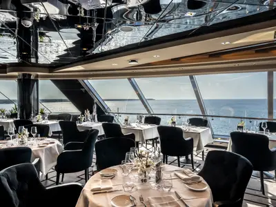 Das elegante Restaurant an Bord der MSC Euribia bietet Tische und Stühle in Schwarz und Weiss, umgeben von grossen Fenstern mit weitem Meerblick.