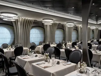 Innenansicht des stilvollen Restaurants Aurora Boreale an Bord der MSC Euribia mit zahlreichen gedeckten Tischen, schwarzen Stühlen und runden Fenstern. Indirekte Beleuchtung und elegante Deckengestaltung prägen den Raum.