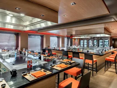 Modernes Kaito Teppanyaki Spezialitätenrestaurant an Bord der MSC Euribia. Theken mit Grillplatten, orangefarbene Stühle und gedeckte Tische laden zum Essen ein.