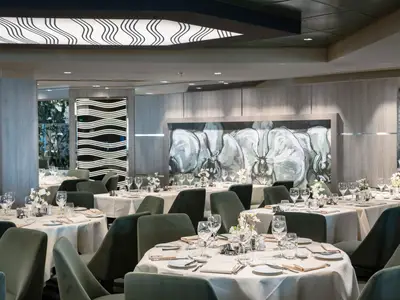 Elegantes Restaurant Green Orchid an Bord der MSC Euribia. Weiß gedeckte Tische, olivgrüne Stühle. Wandbild mit Blütenmotiven.