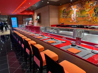 Die rot-orange gestaltete Sushi-Bar Kaito an Bord der MSC Euribia mit modernen Barhockern vor der Zubereitungstheke.