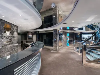 Empfangsbereich des luxuriösen MSC Yacht Club Concierge Area an Bord der MSC Euribia, mit Marmorwänden, eleganter Rezeption und gläserner Wendeltreppe.
