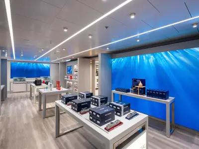 Ein heller, moderner Shop an Bord der MSC Euribia, mit Auslagen von Produkten und Schiffsmodellen. Große Bildschirme zeigen Unterwasserbilder. Das Geschäft ist leer.