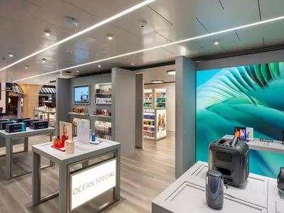 Shopping-Galerie der MSC Euribia mit hellem Ambiente. Auslagen zeigen Parfüms, Kosmetik und Elektronik. Eine große LED-Wand ist sichtbar.