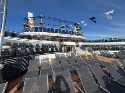 Blick auf das sonnige Außendeck an Bord der MSC Euribia mit zahlreichen leeren Liegestühlen und einem Kletterparcours im Hintergrund.