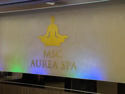 Ein Schild des MSC Aurea Spa mit einer goldenen, meditierenden Figur auf einer Wasserwand an Bord der MSC Euribia.