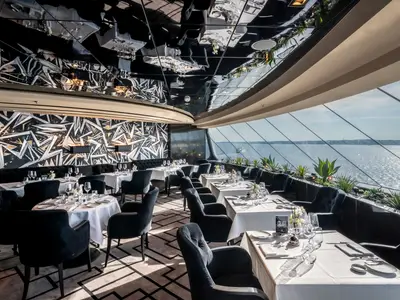 Ein luxuriöses Restaurant an Bord der MSC Euribia mit großen Panoramafenstern und Meerblick. Der Raum ist mit gedeckten Tischen, eleganten Stühlen und einer schwarz-weiß gemusterten Wand ausgestattet. Die Decke spiegelt den Raum wider.